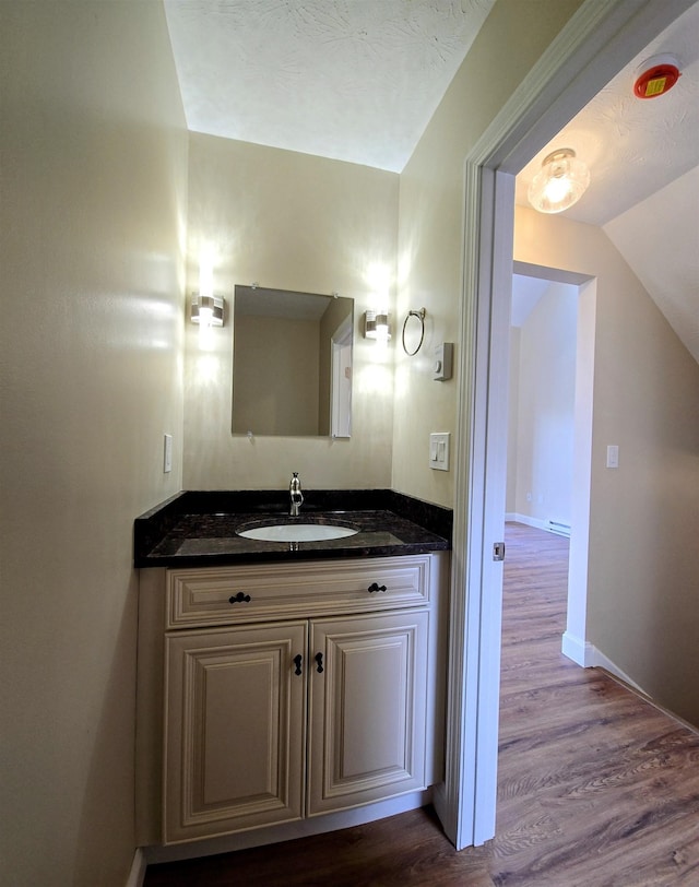 bathroom featuring vaulted ceiling, wood finished floors, vanity, and baseboards