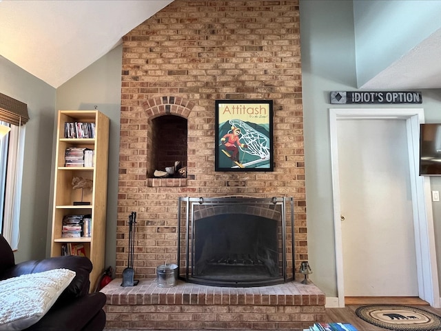 living room featuring lofted ceiling, a brick fireplace, and wood finished floors