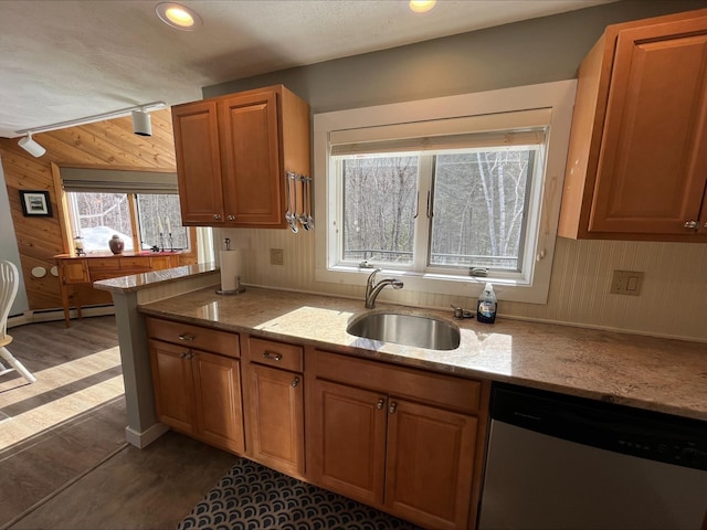 kitchen featuring brown cabinets, stainless steel dishwasher, wood walls, a baseboard heating unit, and a sink