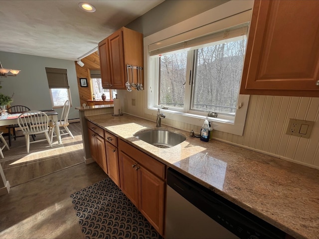 kitchen with brown cabinetry, light stone counters, a sink, stainless steel dishwasher, and recessed lighting