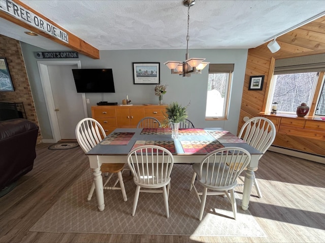 dining room featuring a notable chandelier, a baseboard heating unit, wooden walls, a textured ceiling, and wood finished floors