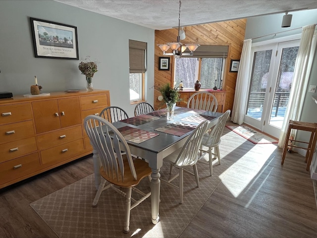 dining room featuring wooden walls, dark wood finished floors, vaulted ceiling, a textured ceiling, and a notable chandelier