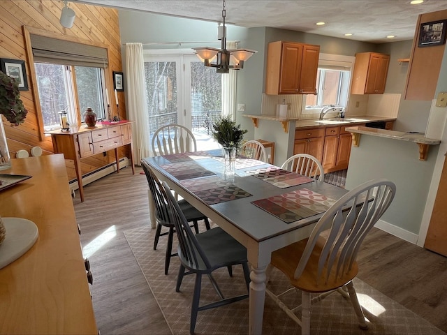 dining area with wooden walls, wood finished floors, baseboard heating, a chandelier, and recessed lighting