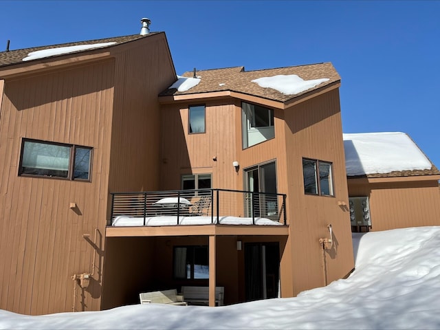 snow covered rear of property with a balcony