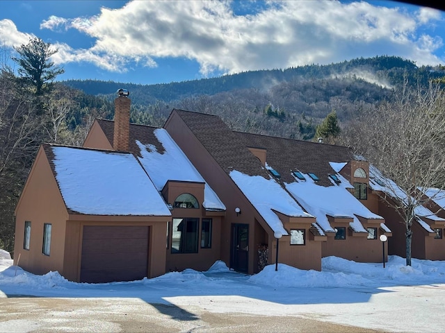 view of front facade featuring an attached garage, a forest view, a chimney, and stucco siding