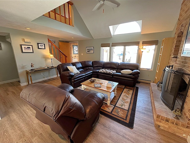 living room featuring light wood finished floors, baseboard heating, a brick fireplace, baseboards, and stairs