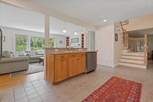 kitchen featuring pendant lighting, stainless steel dishwasher, open floor plan, light tile patterned flooring, and a sink