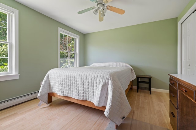 bedroom with a baseboard radiator, a closet, a ceiling fan, light wood-type flooring, and baseboards