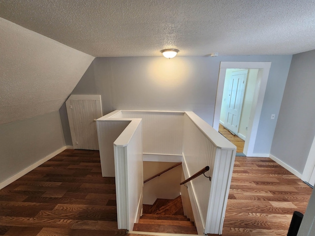 stairs with vaulted ceiling, a textured ceiling, wood finished floors, and baseboards