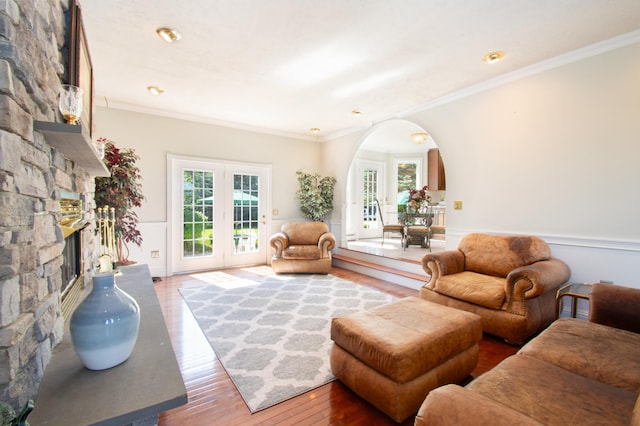 living area featuring arched walkways, ornamental molding, wainscoting, a stone fireplace, and hardwood / wood-style floors