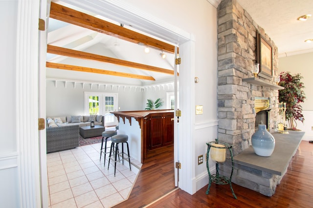 kitchen with vaulted ceiling with beams, a breakfast bar, wood finished floors, and a stone fireplace