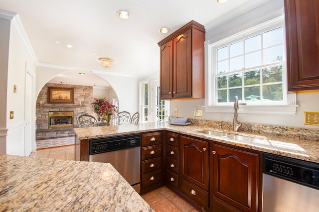 kitchen with crown molding, dishwasher, a stone fireplace, and a sink