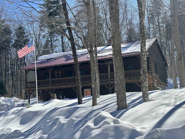 snow covered rear of property with metal roof and log veneer siding