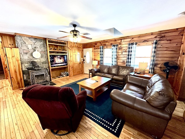 living area with a skylight, a ceiling fan, hardwood / wood-style flooring, a wood stove, and wood walls