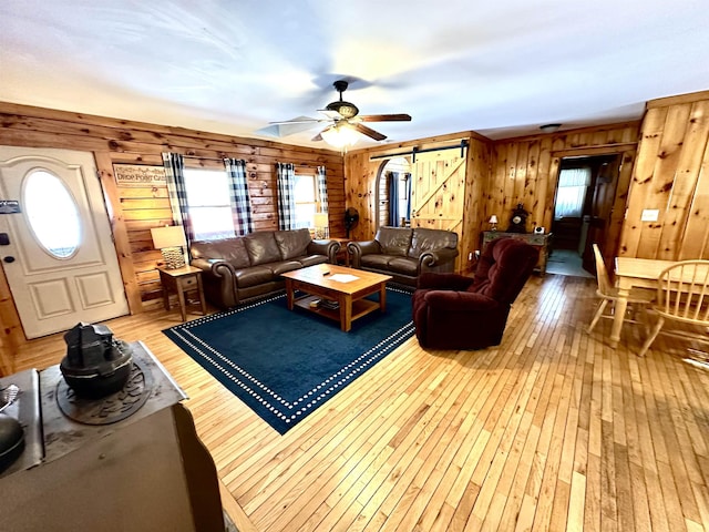 living area featuring light wood-style floors, a wealth of natural light, wood walls, and a barn door