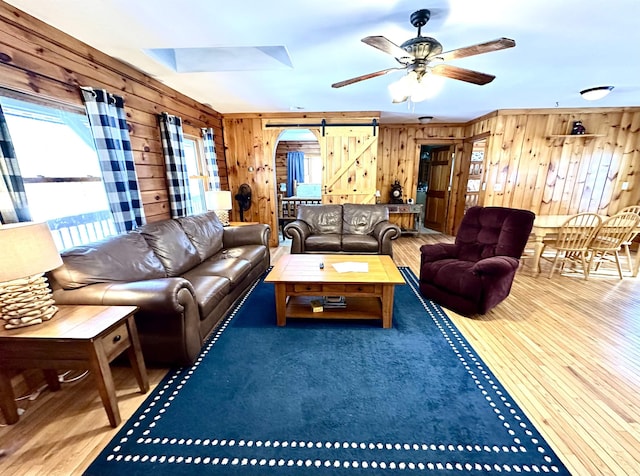 living room with a barn door, wood finished floors, a ceiling fan, and wooden walls