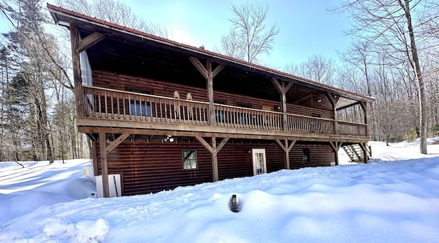 snow covered rear of property featuring log veneer siding and a wooden deck