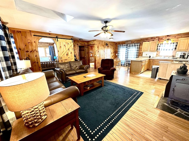 living area with plenty of natural light, a barn door, light wood-type flooring, and a ceiling fan