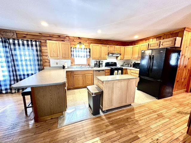 kitchen with light countertops, a sink, light wood-type flooring, a peninsula, and black appliances