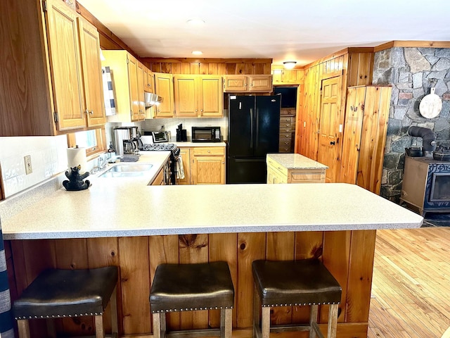 kitchen featuring a breakfast bar area, a peninsula, light countertops, black appliances, and a sink