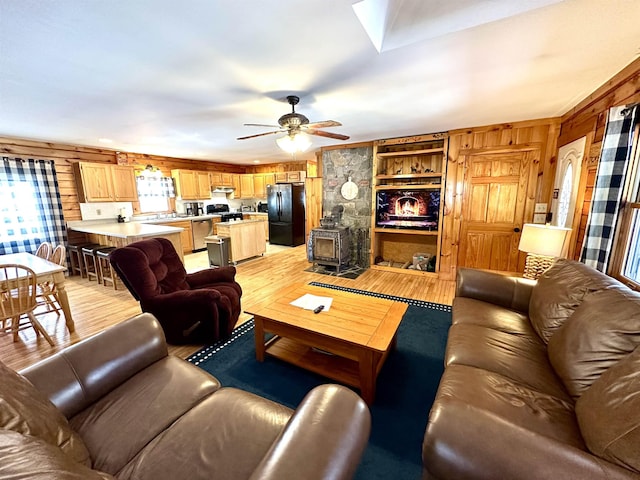 living area with a ceiling fan, a skylight, light wood-style flooring, and wooden walls