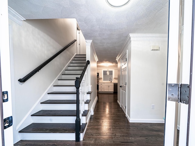 staircase featuring a textured ceiling, ornamental molding, wood finished floors, and baseboards