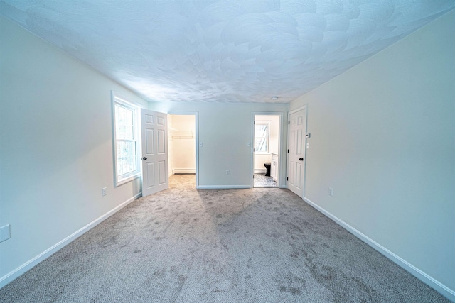 unfurnished bedroom with a textured ceiling, multiple windows, baseboards, and carpet flooring