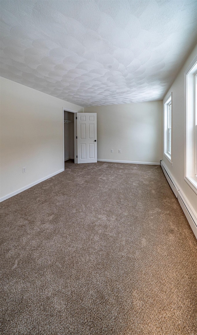 unfurnished room featuring a textured ceiling, baseboard heating, carpet, and baseboards