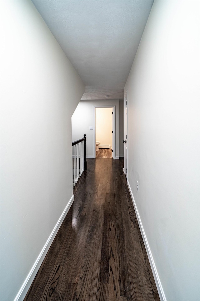 hall featuring dark wood-type flooring, an upstairs landing, and baseboards