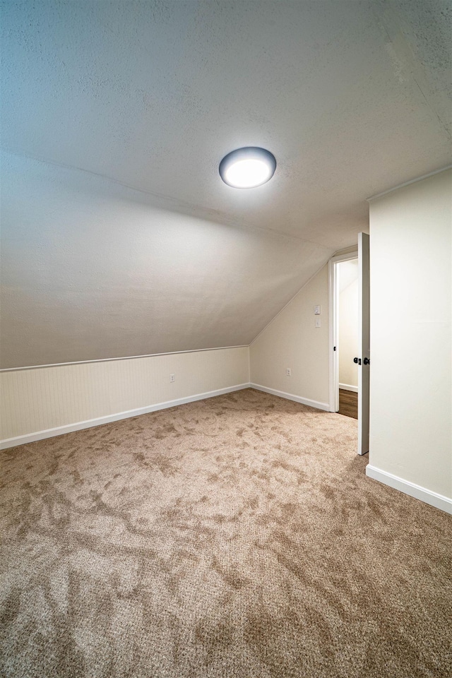 additional living space with a textured ceiling, carpet floors, vaulted ceiling, and baseboards