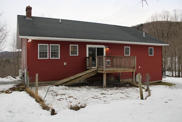 snow covered house featuring roof with shingles, a chimney, a wooden deck, and stairs