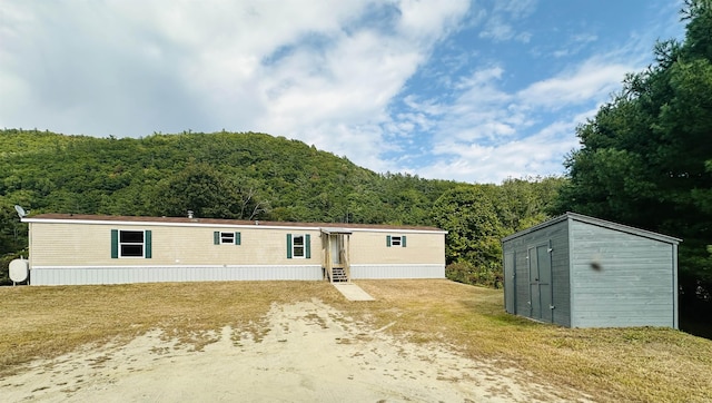 view of front of home with entry steps, an outdoor structure, a wooded view, and a storage shed