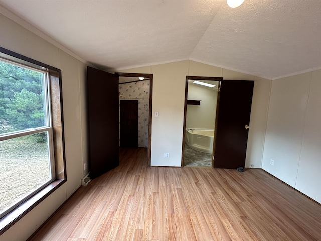 unfurnished bedroom featuring vaulted ceiling, light wood finished floors, a textured ceiling, and connected bathroom