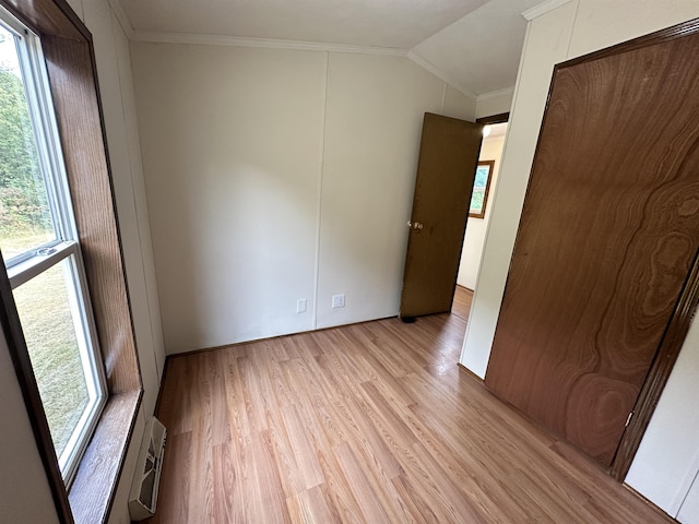 unfurnished bedroom with vaulted ceiling, ornamental molding, multiple windows, and light wood-style floors