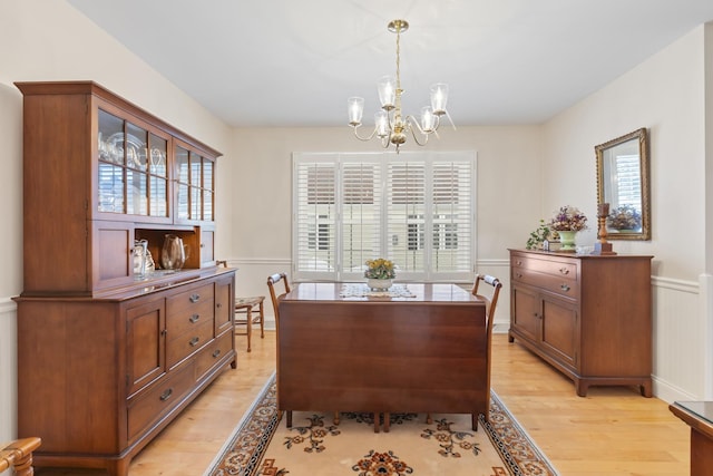 dining space with light wood finished floors, wainscoting, and a notable chandelier