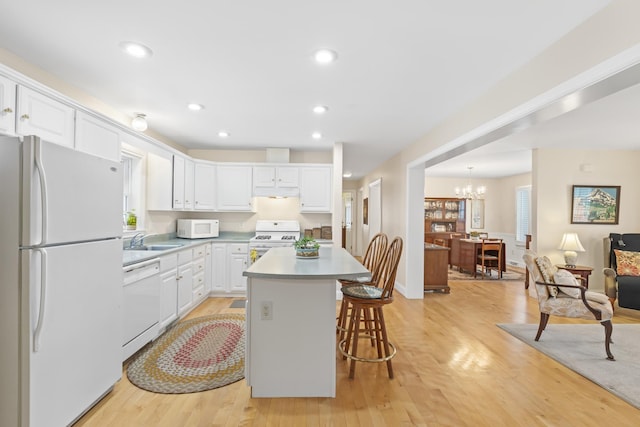 kitchen featuring light wood-style flooring, white appliances, a kitchen island, a sink, and white cabinetry