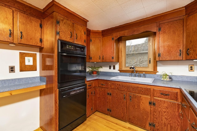 kitchen with black appliances, brown cabinetry, light wood-type flooring, and a sink