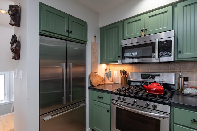 kitchen featuring appliances with stainless steel finishes, dark countertops, backsplash, and green cabinetry