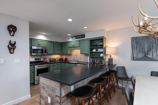 kitchen featuring light wood finished floors, green cabinetry, appliances with stainless steel finishes, backsplash, and a sink