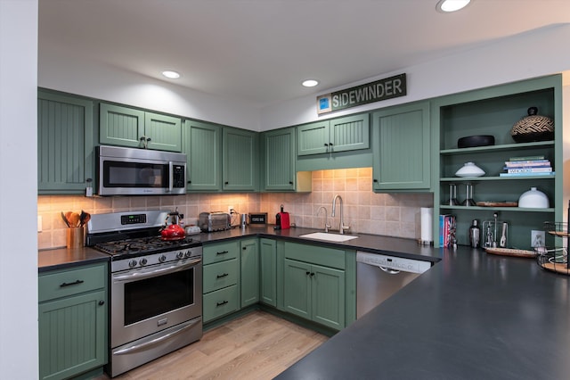 kitchen with tasteful backsplash, dark countertops, appliances with stainless steel finishes, a sink, and green cabinetry