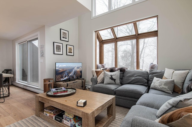 living area featuring a towering ceiling, light wood-style flooring, and baseboard heating