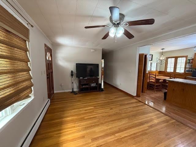 unfurnished living room with light wood-style flooring, a baseboard heating unit, ornamental molding, ceiling fan, and baseboards