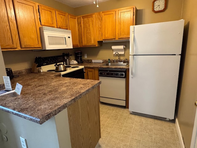 kitchen featuring a peninsula, white appliances, a sink, light floors, and dark countertops