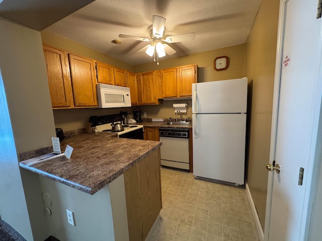 kitchen with a textured ceiling, a peninsula, white appliances, a sink, and dark countertops