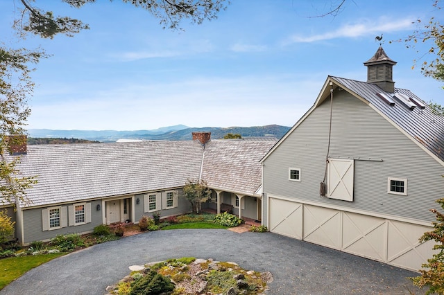 view of front of property with driveway, a garage, a chimney, a standing seam roof, and a mountain view