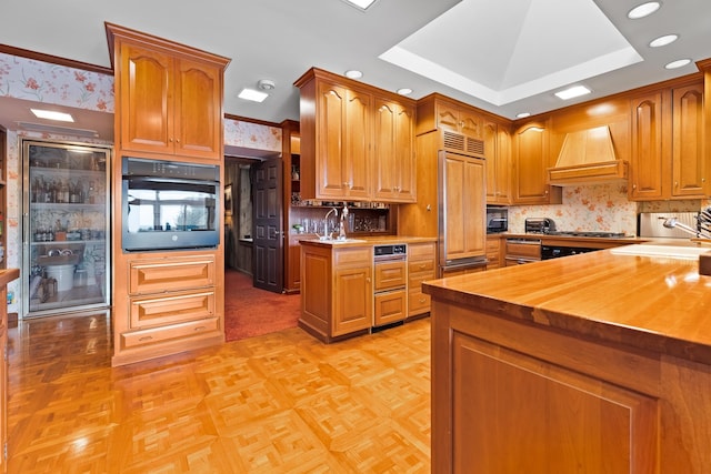 kitchen with wallpapered walls, butcher block countertops, premium range hood, a sink, and black oven