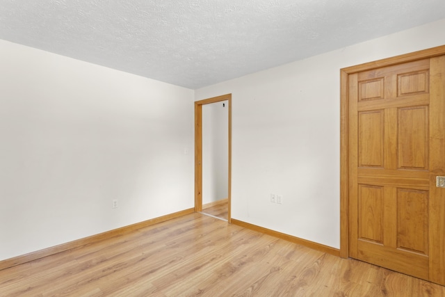 empty room with a textured ceiling, light wood-style flooring, and baseboards