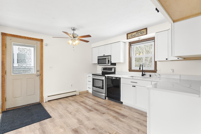 kitchen featuring a baseboard heating unit, a wealth of natural light, a sink, and appliances with stainless steel finishes