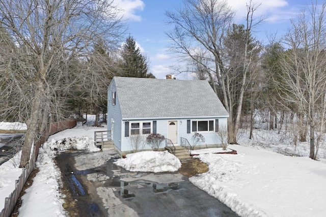 new england style home with a shingled roof, a chimney, and aphalt driveway