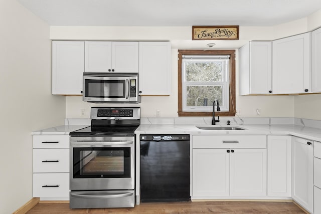 kitchen with light stone counters, appliances with stainless steel finishes, white cabinets, and a sink